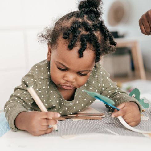 Toddler drawing with colored pencils at a table, focused on a sheet of paper