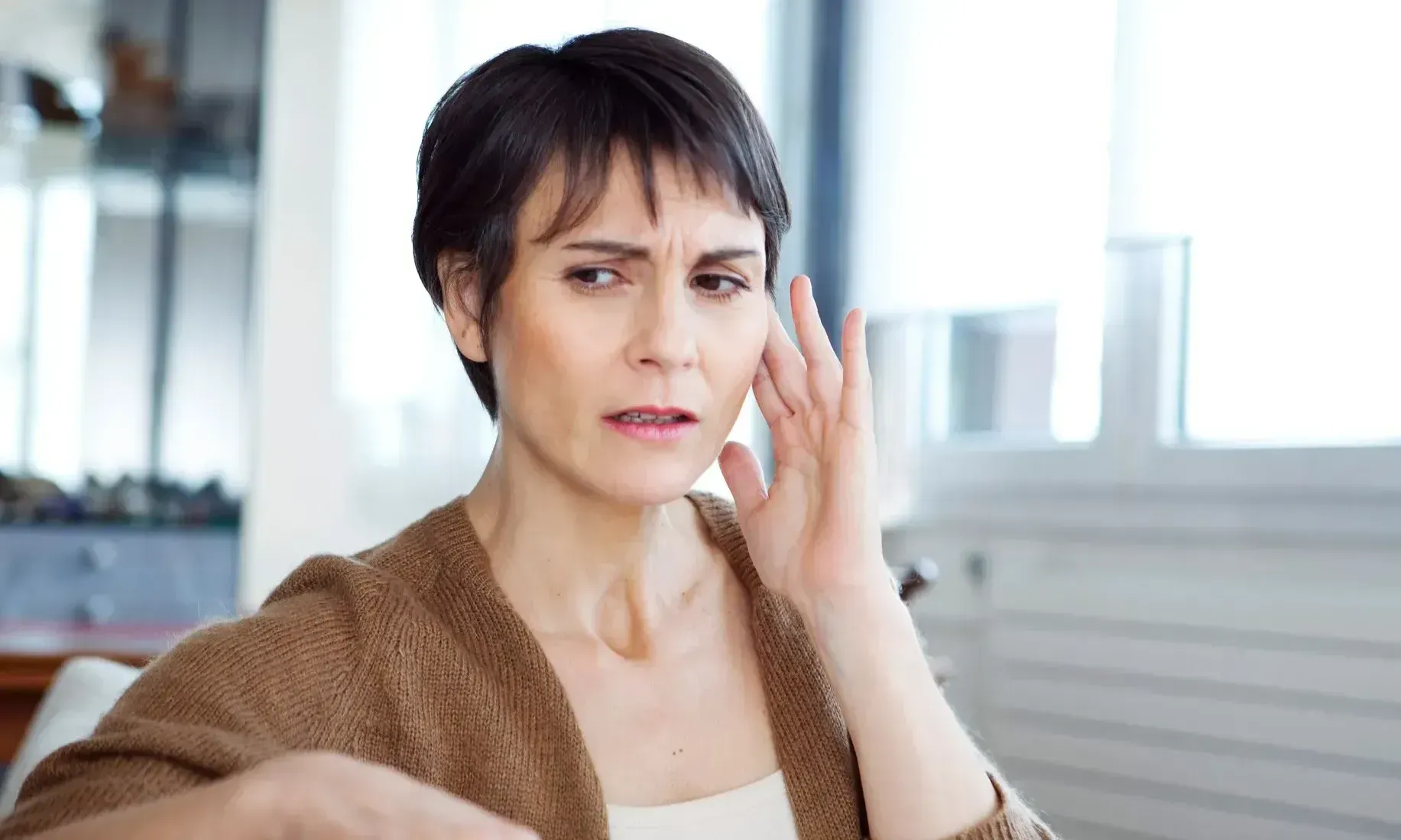 A woman is holding her hand to her ear.