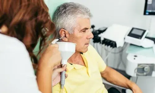 An elderly man is sitting in a chair while a woman holds a device to his face.