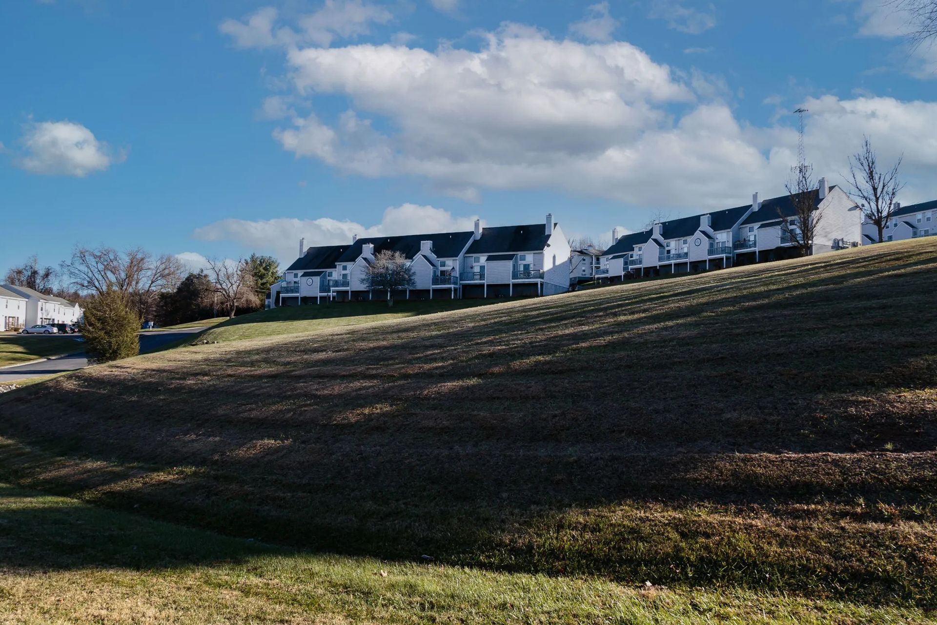 Row of white townhouses on a grassy hill under a blue sky with clouds.