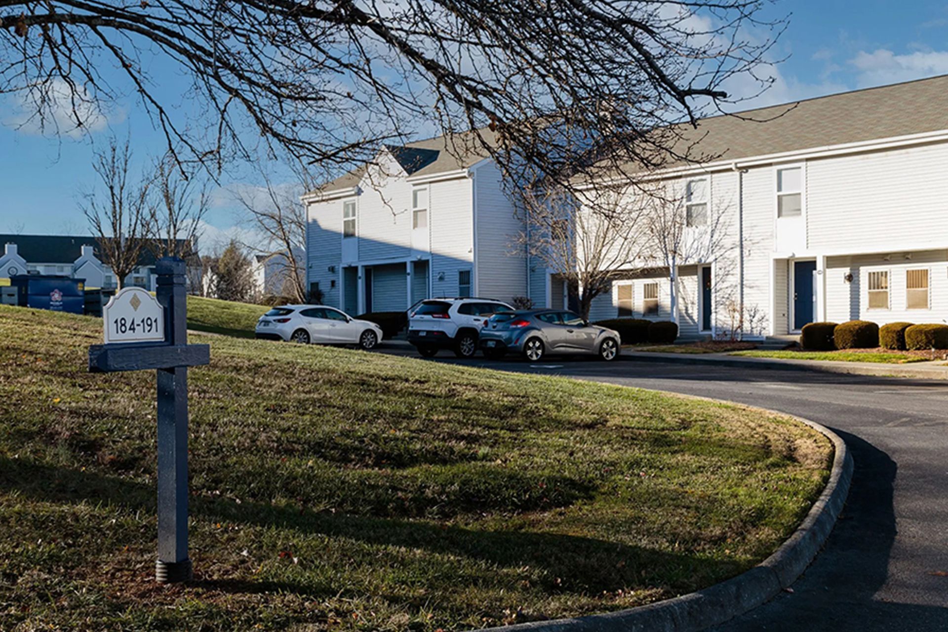 Apartment buildings with cars parked out front on a sunny day. Sign in foreground.