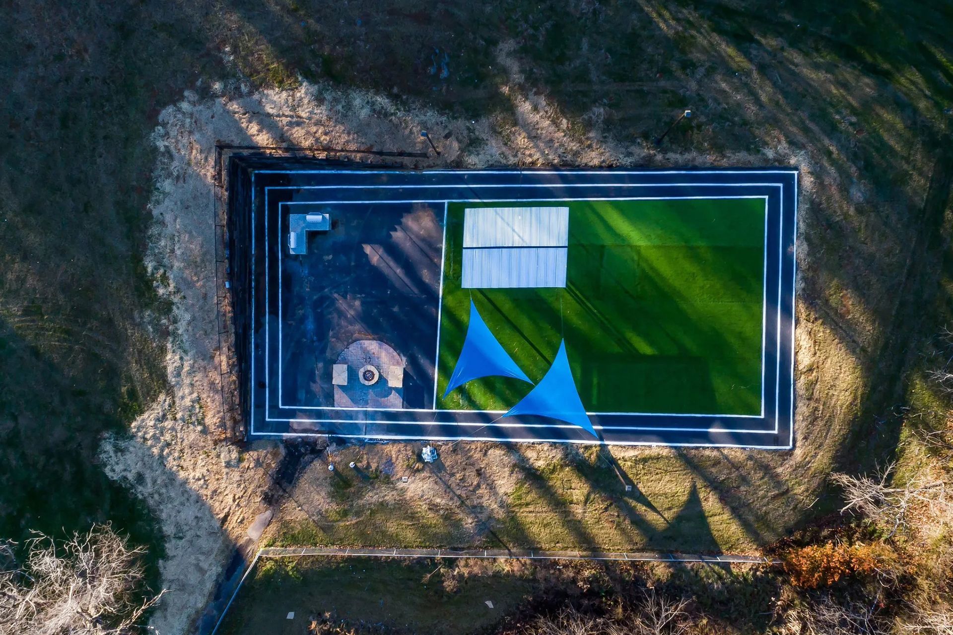 Aerial view of an outdoor recreational area with artificial turf, blue shade sails, and a small shelter.