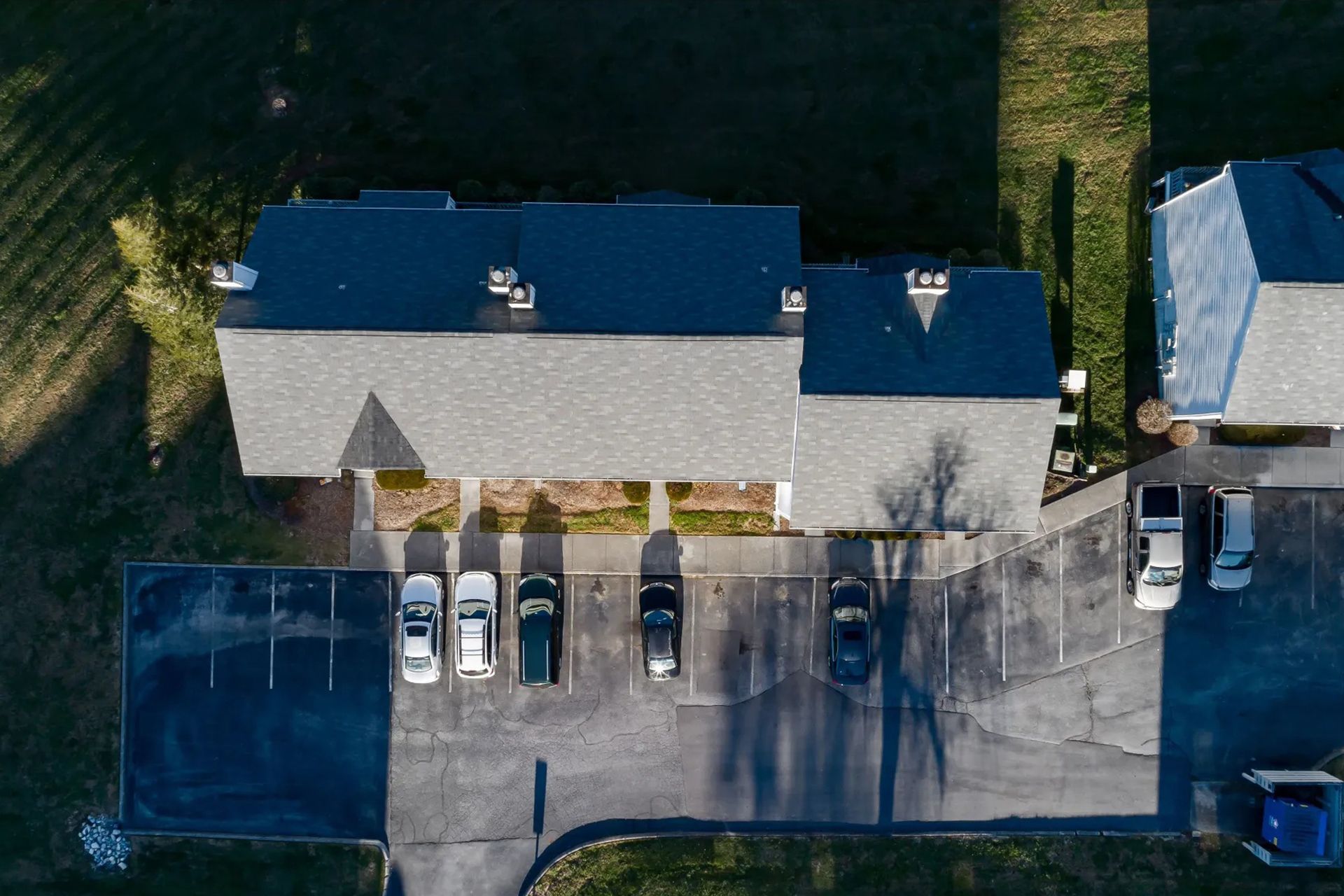 Overhead view of a building with a grey roof and parking lot filled with cars.