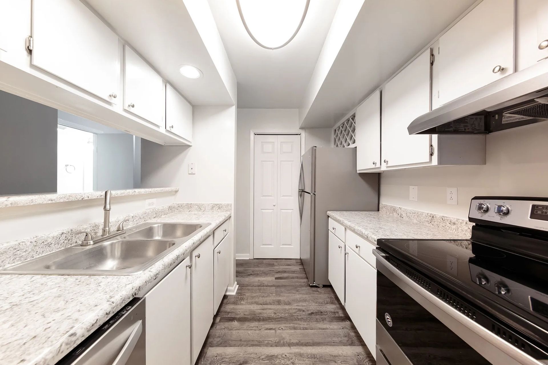 Narrow kitchen with white cabinets, countertops, stainless steel appliances, and gray flooring.