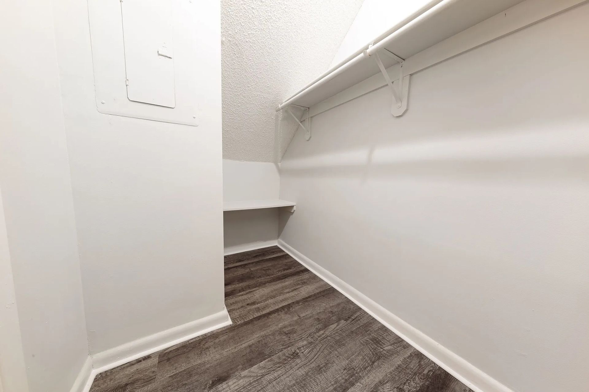 Empty white closet with wood-look flooring, a shelf, and a small built-in shelf.