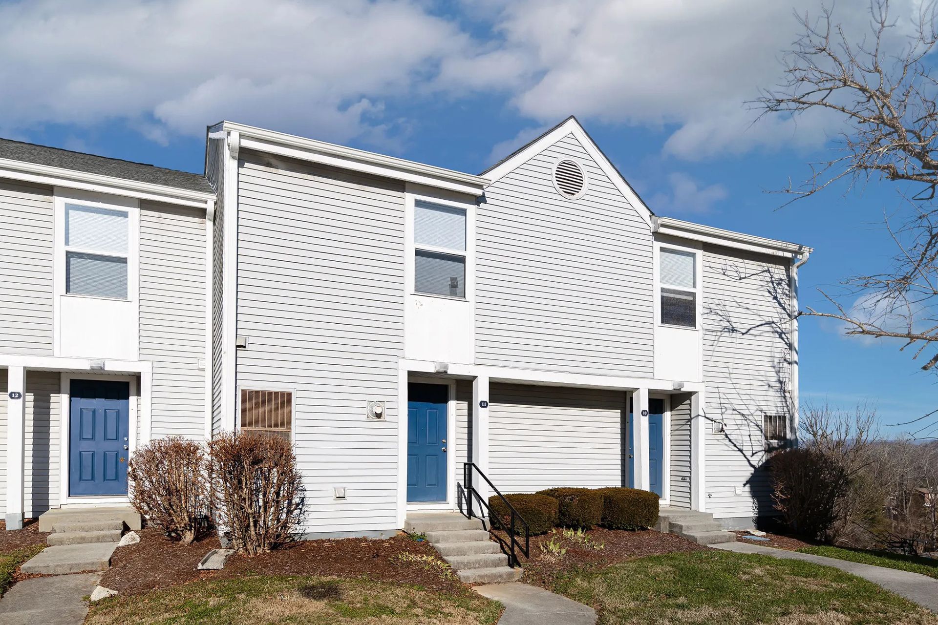 Townhomes with white siding, blue doors, and a clear sky.