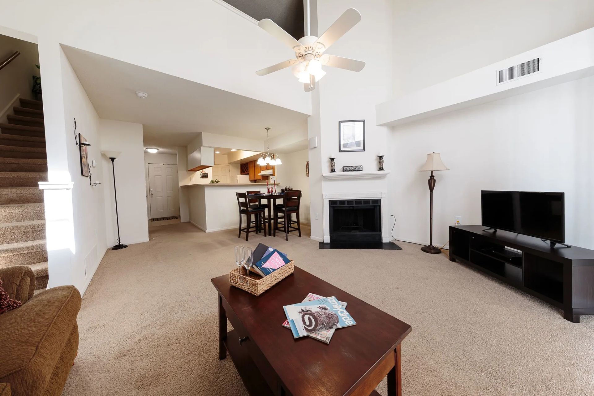 Living room with stairs, fireplace, kitchen, brown furniture, and TV.