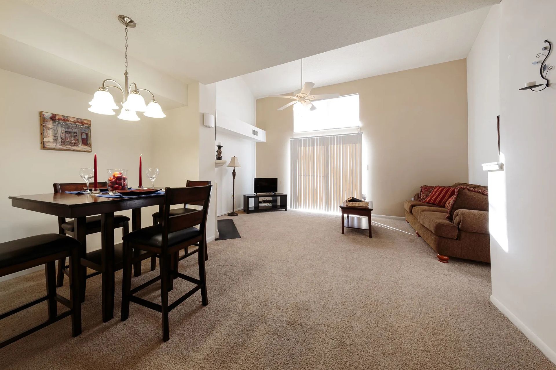 Dining room with a square table and chairs, living room with a couch, and a sliding door.