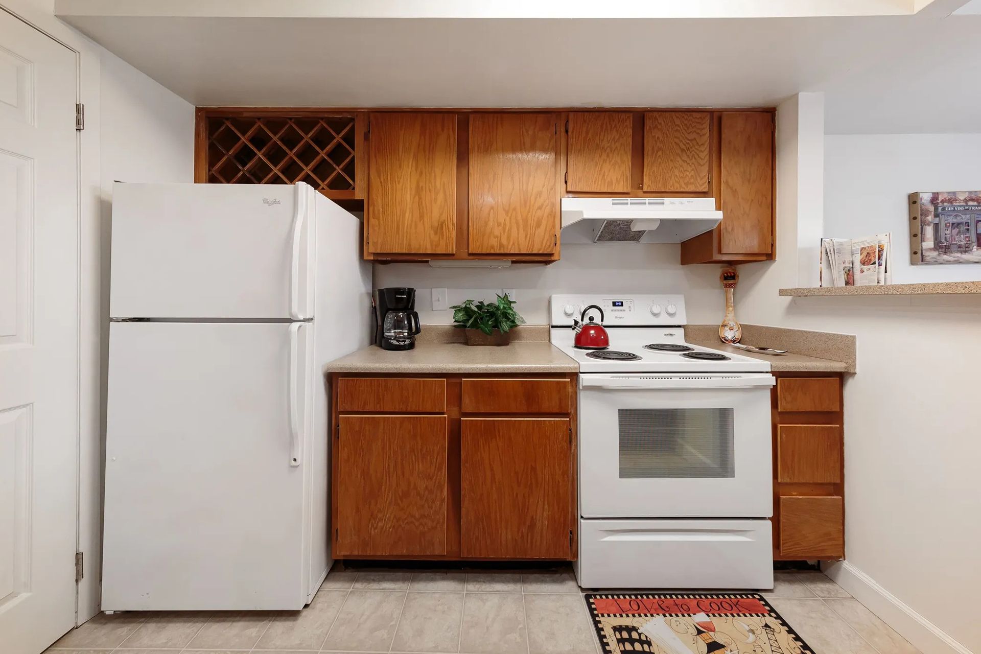 Small kitchen with white appliances and wood cabinets. A red teapot sits on the stove.