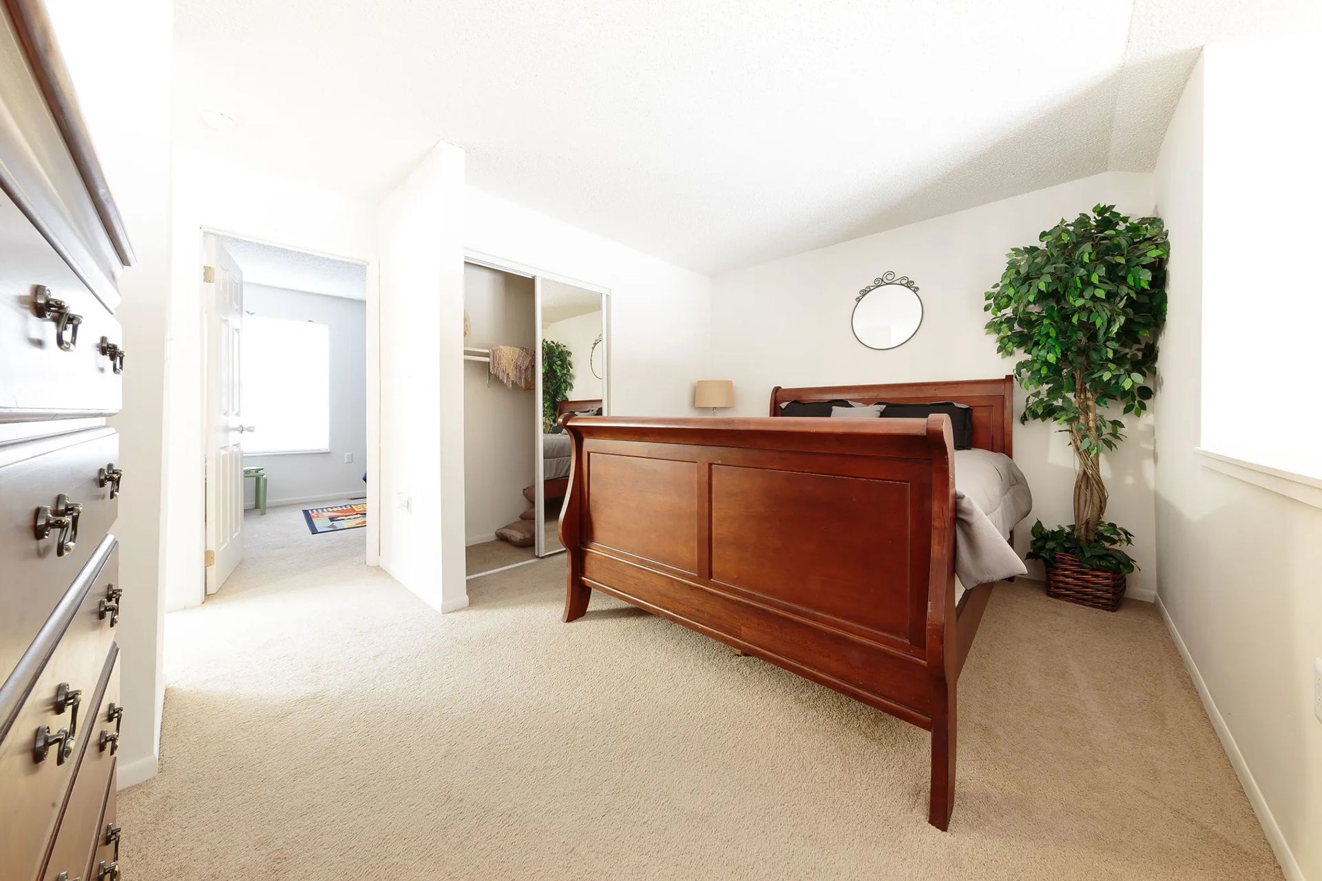 Bedroom with a brown wooden bed, large dresser, and a faux tree.