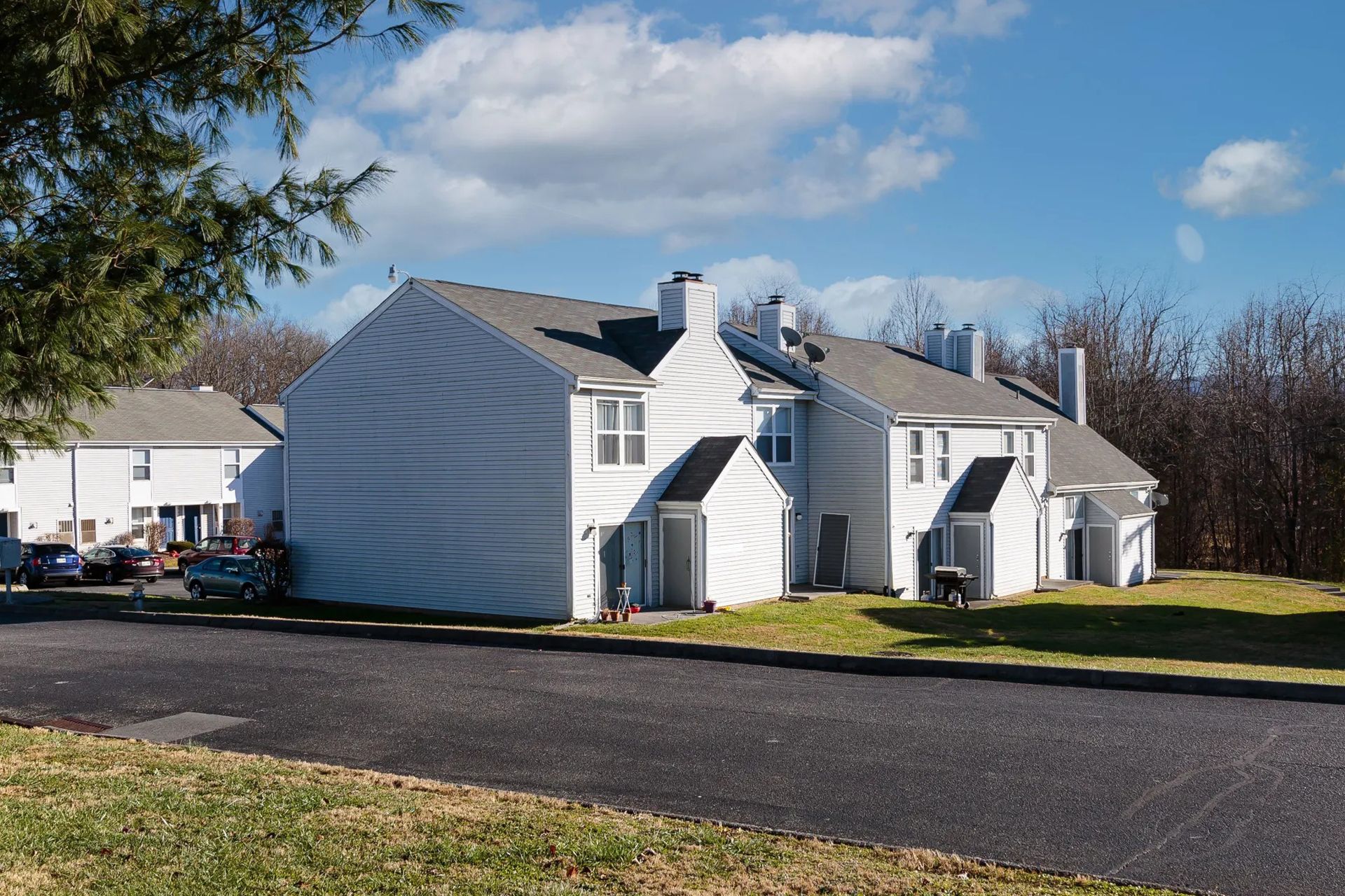 White townhouses on a sunny day with a blue sky and green grass. Black asphalt in the foreground.