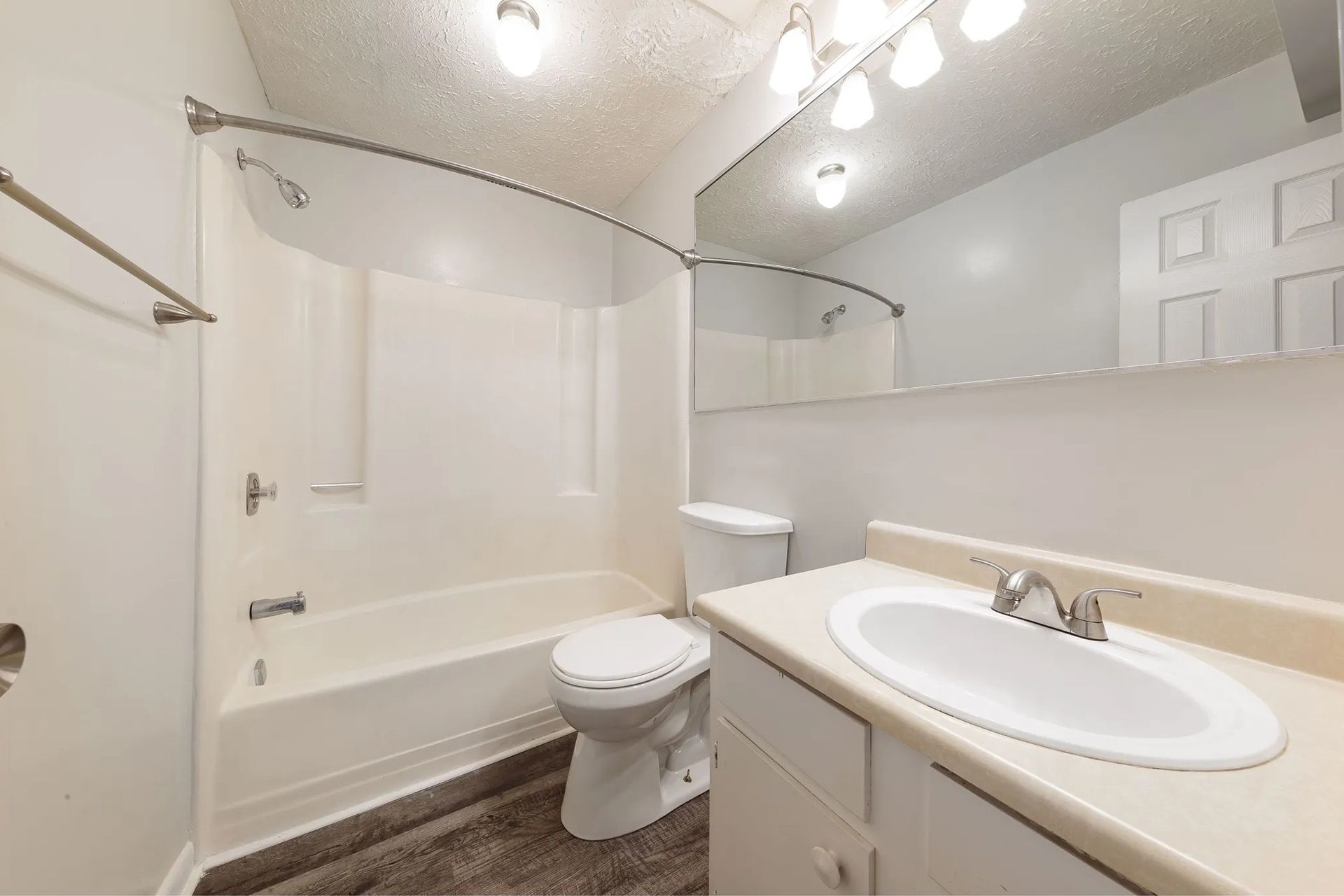 Bathroom with a white tub, toilet, and sink. White cabinets, light gray walls, and a mirror.