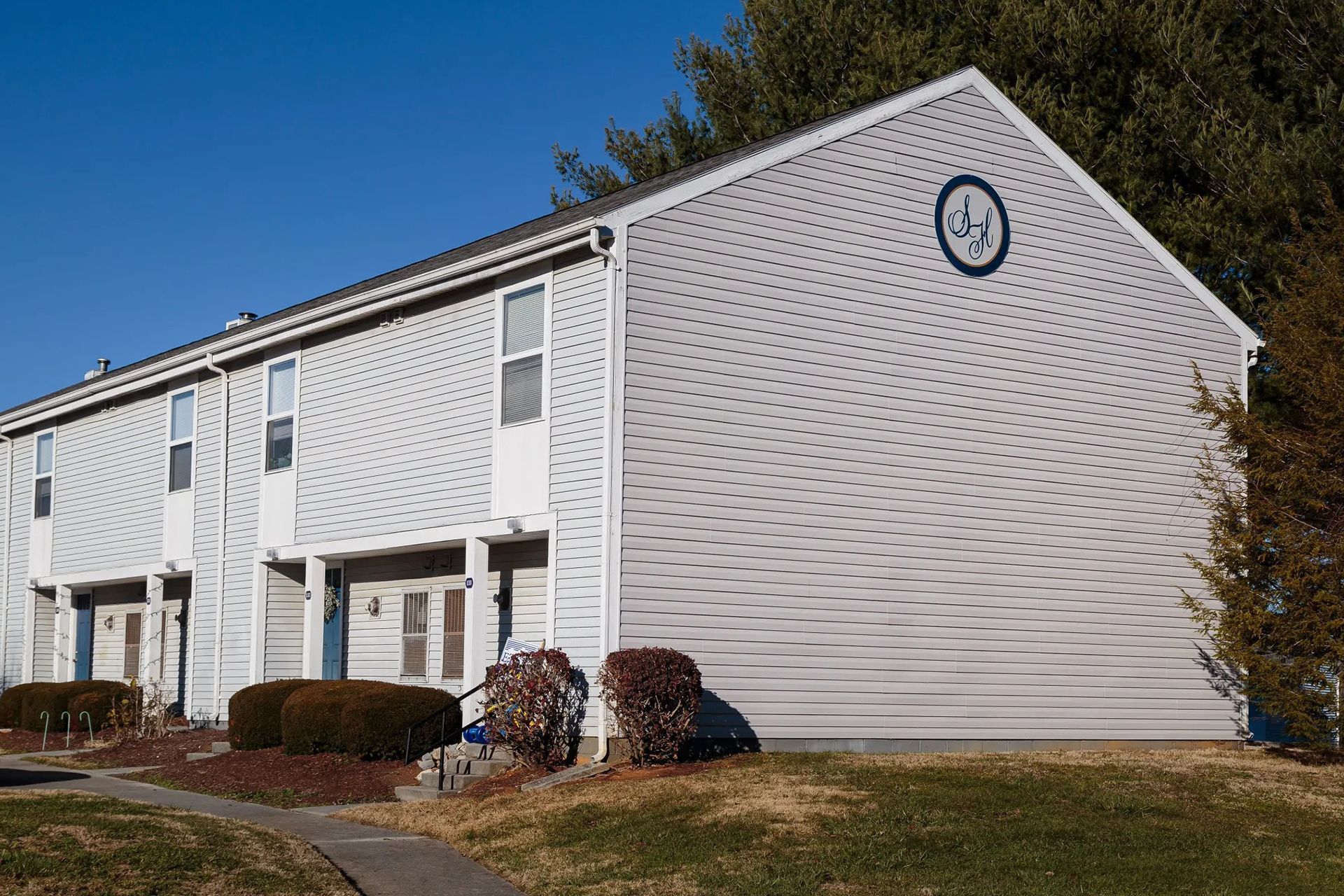 Row of light gray townhomes on a sunny day with bushes and green grass in the foreground.