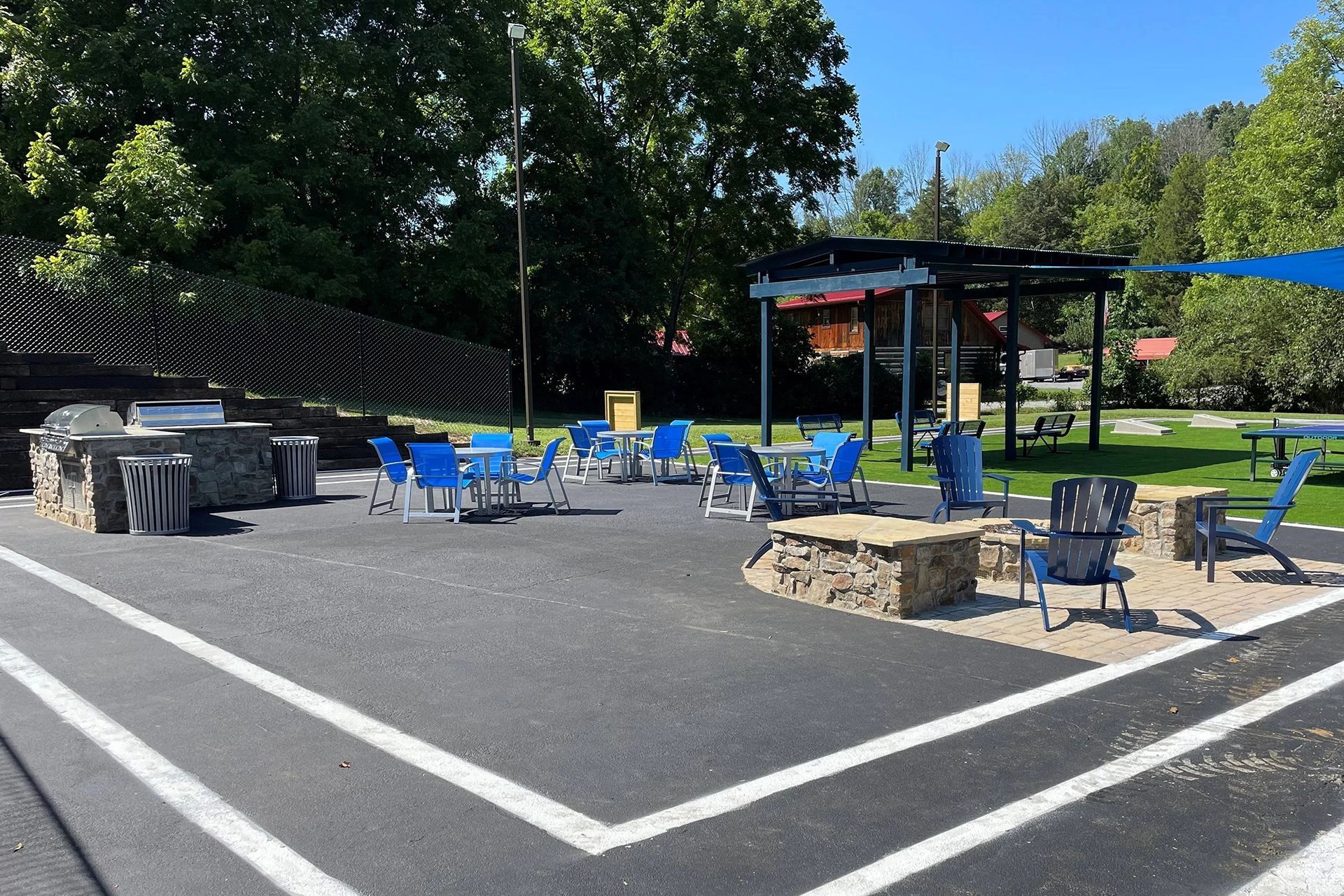 Outdoor patio with blue chairs, grill, fire pit, and pergola on asphalt surface.