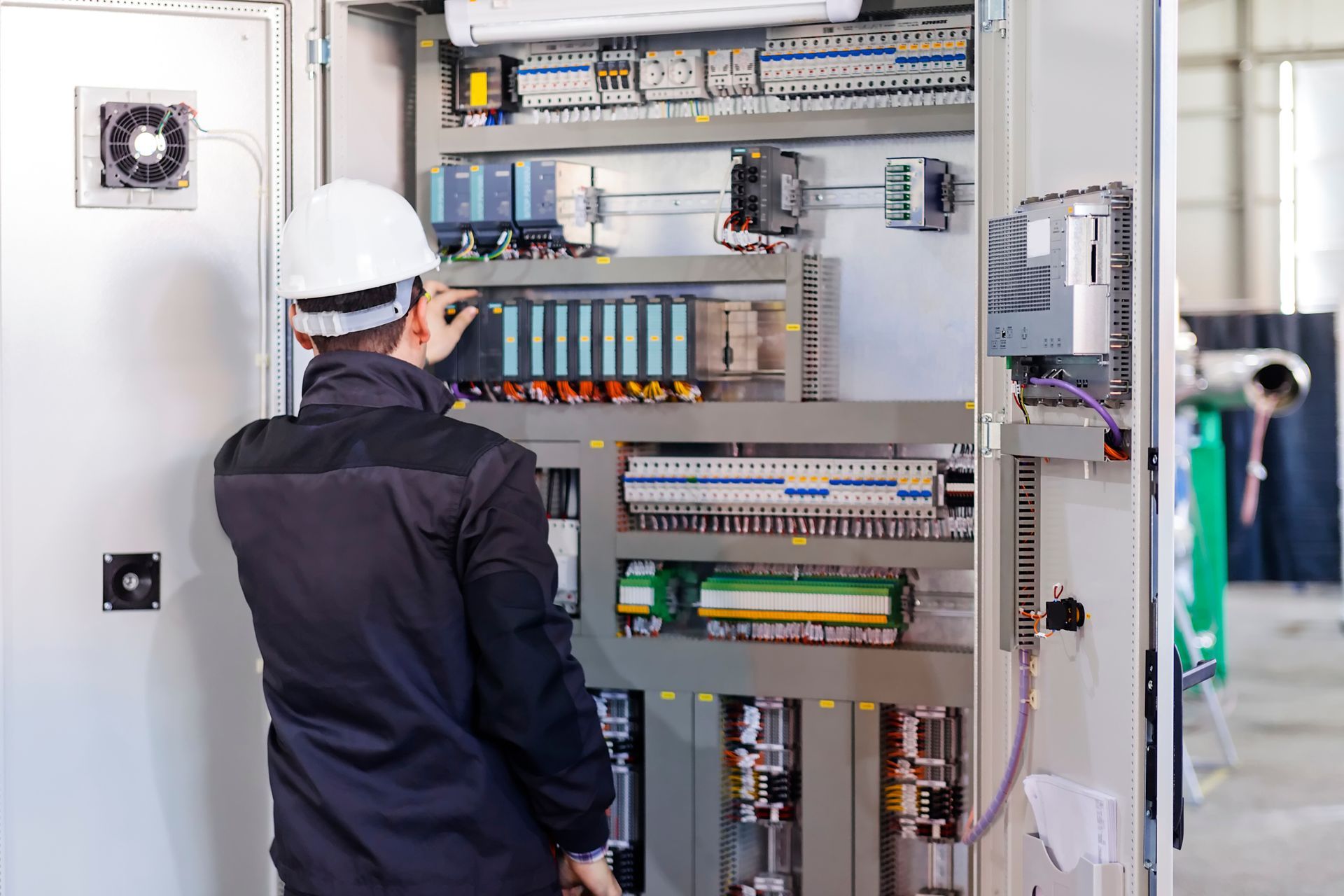 Person in white hard hat working on an electrical control panel.