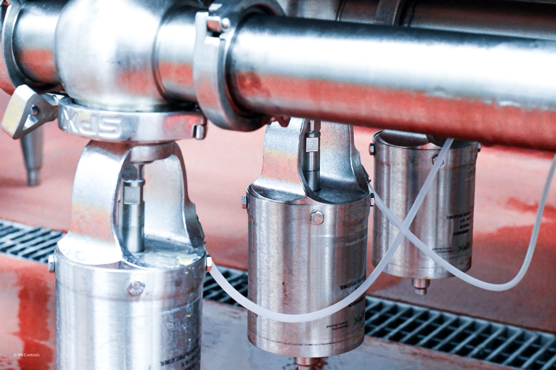 Stainless steel industrial piping with attached cylinders and tubing, likely for liquid processing.