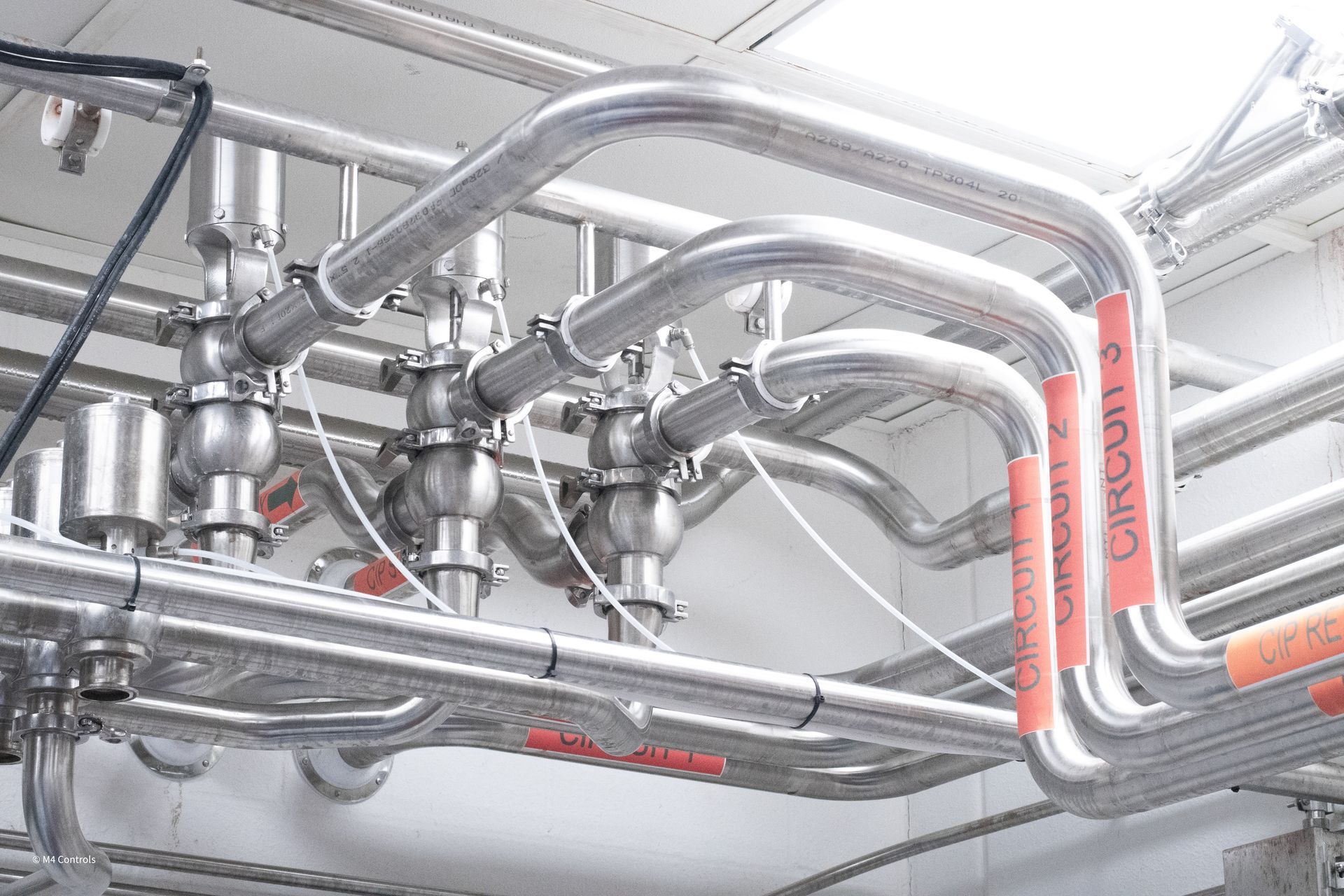 Stainless steel pipes with valves and labeling, indoors.