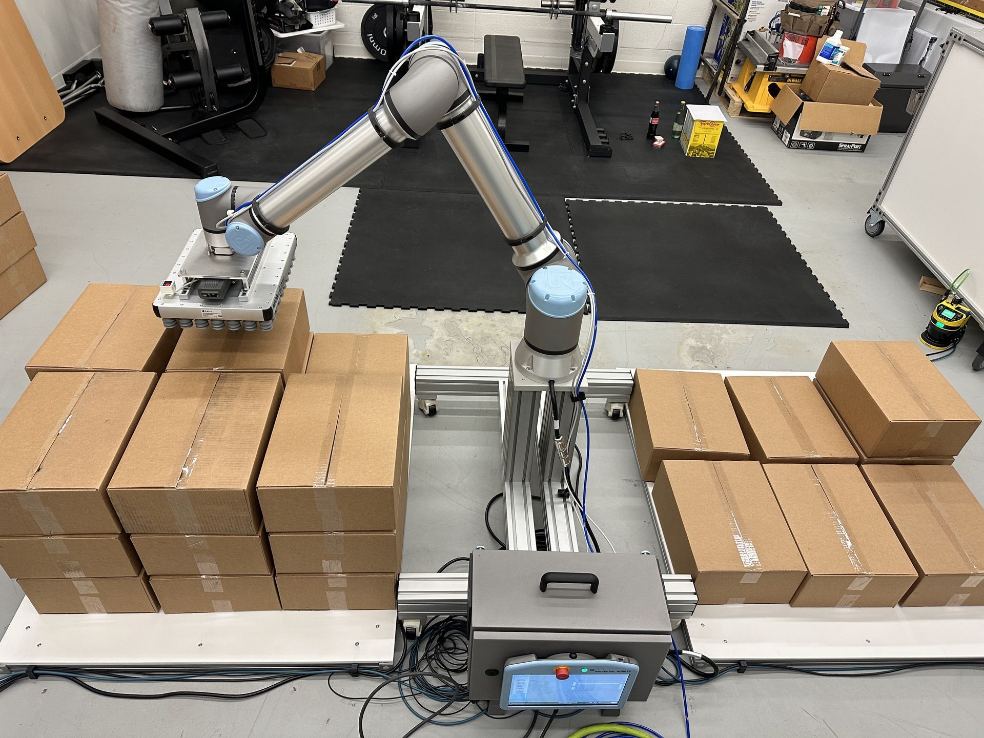 Robot arm picks up a cardboard box from a stack, with others in the setting. Industrial facility.