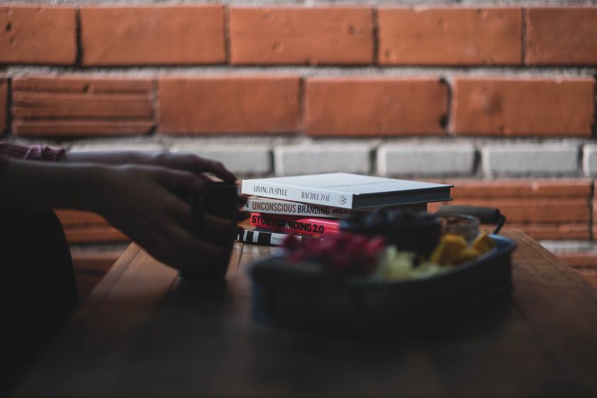 A person is sitting at a table with a stack of books and a bowl of fruit.