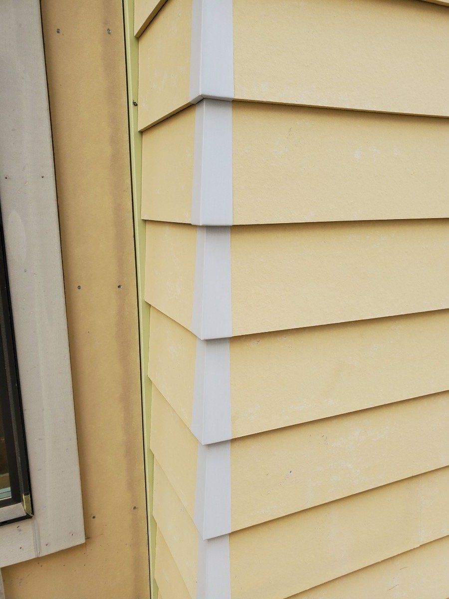 A close up of a yellow siding on a house next to a window.