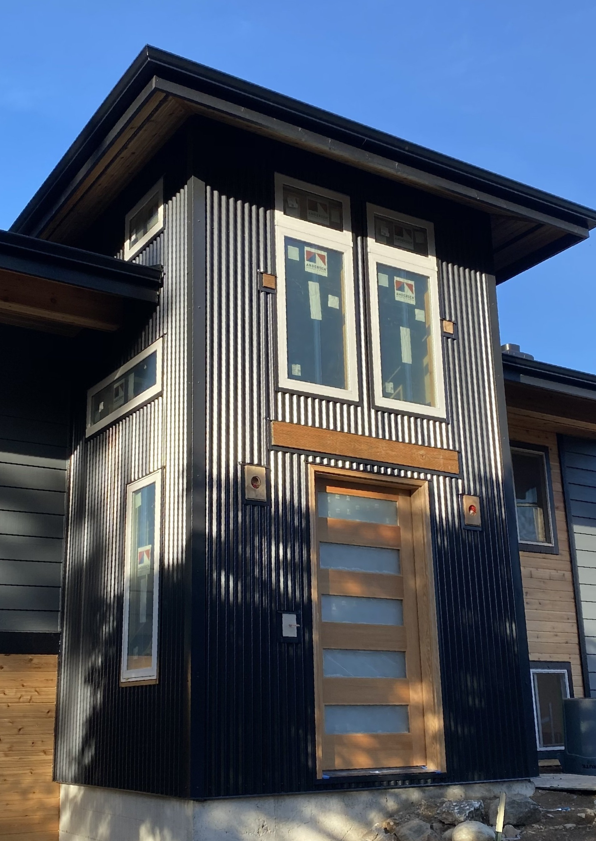 A house with a black siding and a wooden door is being built.