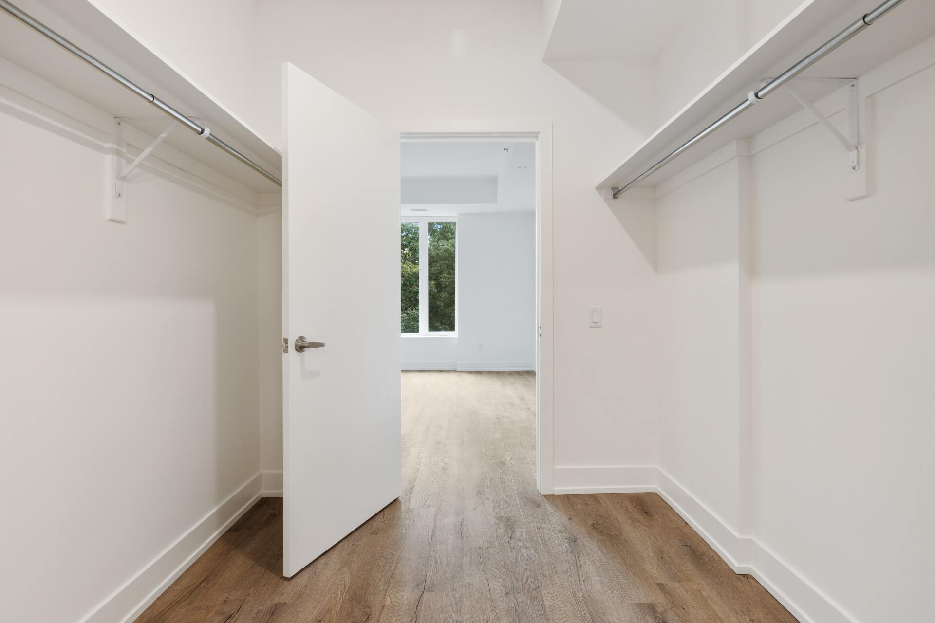 An empty walk in closet with hardwood floors and white walls.