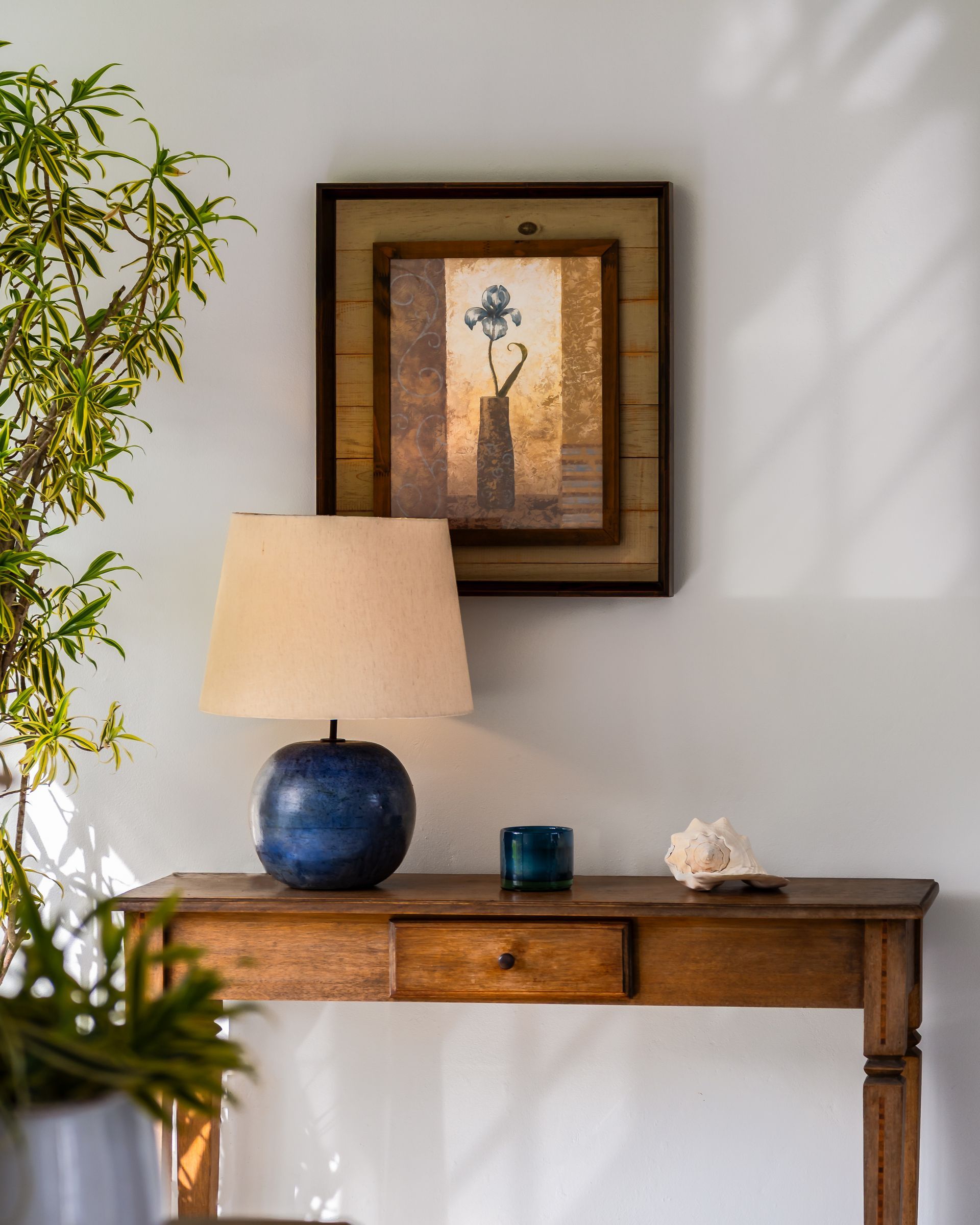 Uma mesa de madeira com um abajur e um quadro na parede acima dela.