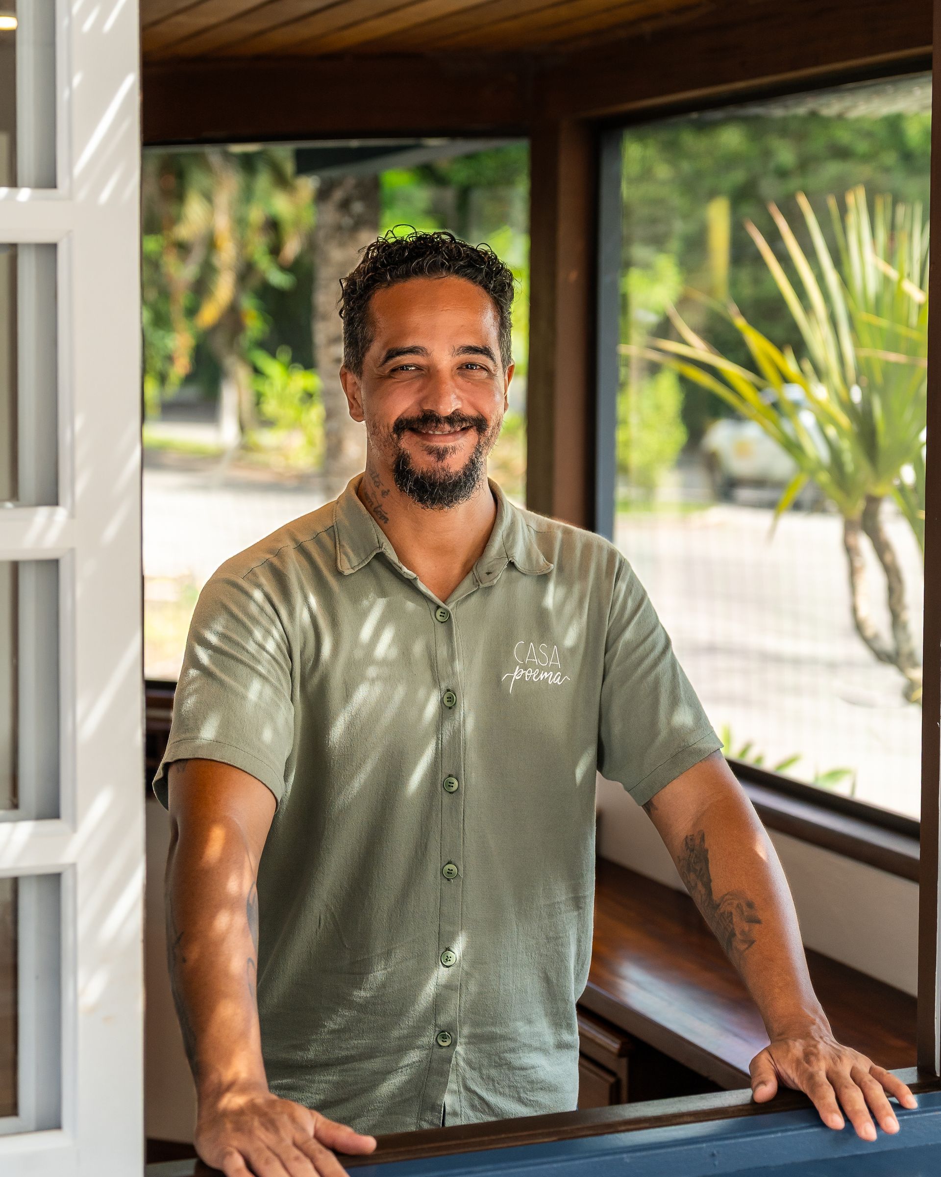 Um homem com barba está parado em frente a uma janela.folha