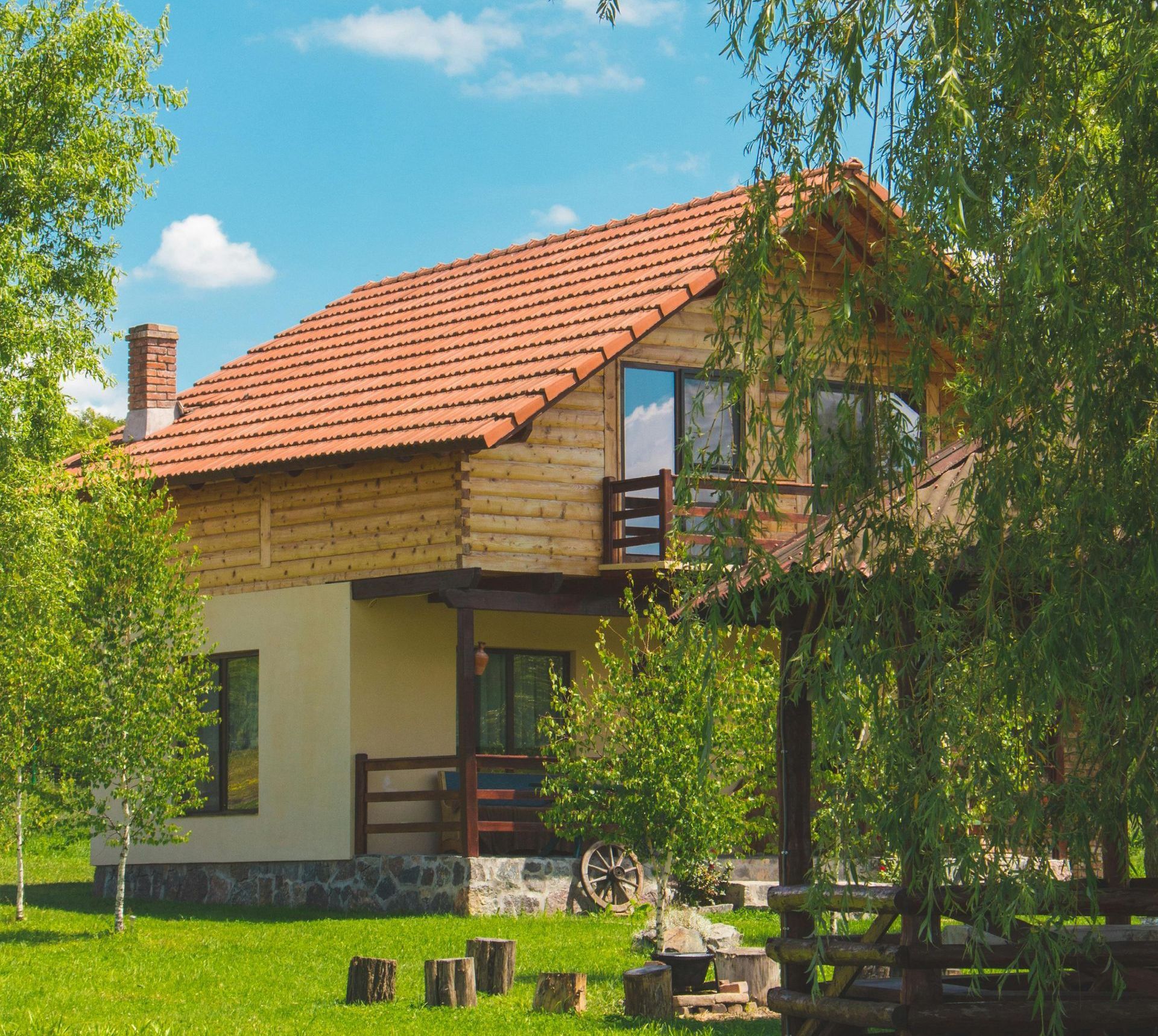 A wooden house with a red tile roof is surrounded by trees and grass.