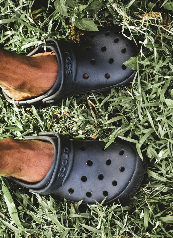A person wearing a pair of black crocs is standing in the grass.