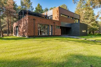 A modern brick house with a large lawn in front of it surrounded by trees.