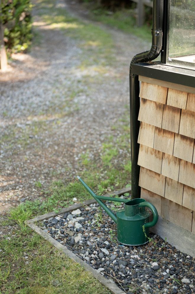 A green watering can is sitting on the ground next to a house.