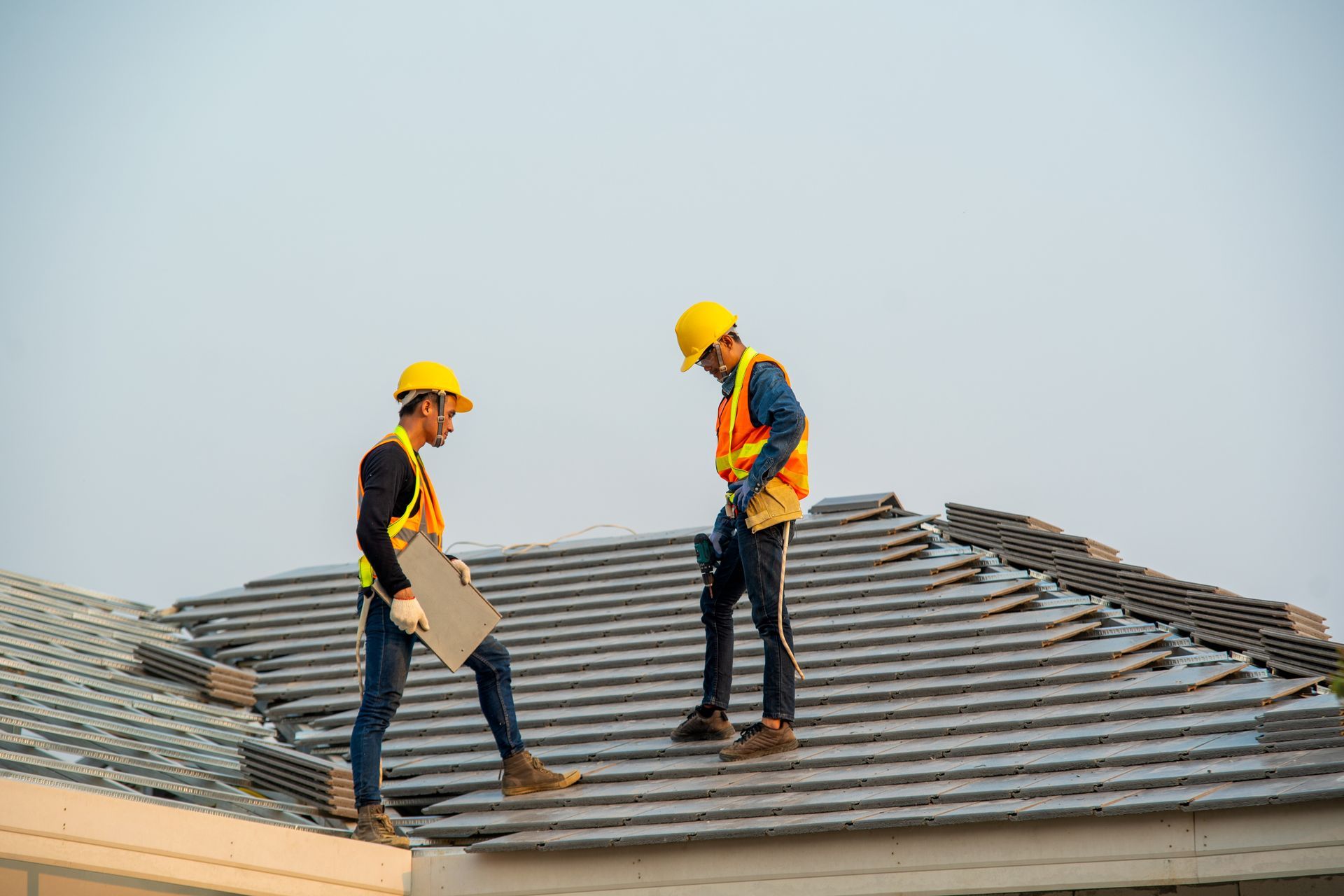 Roofers from a residential roofing company installing new tiles on a house under a clear sky.