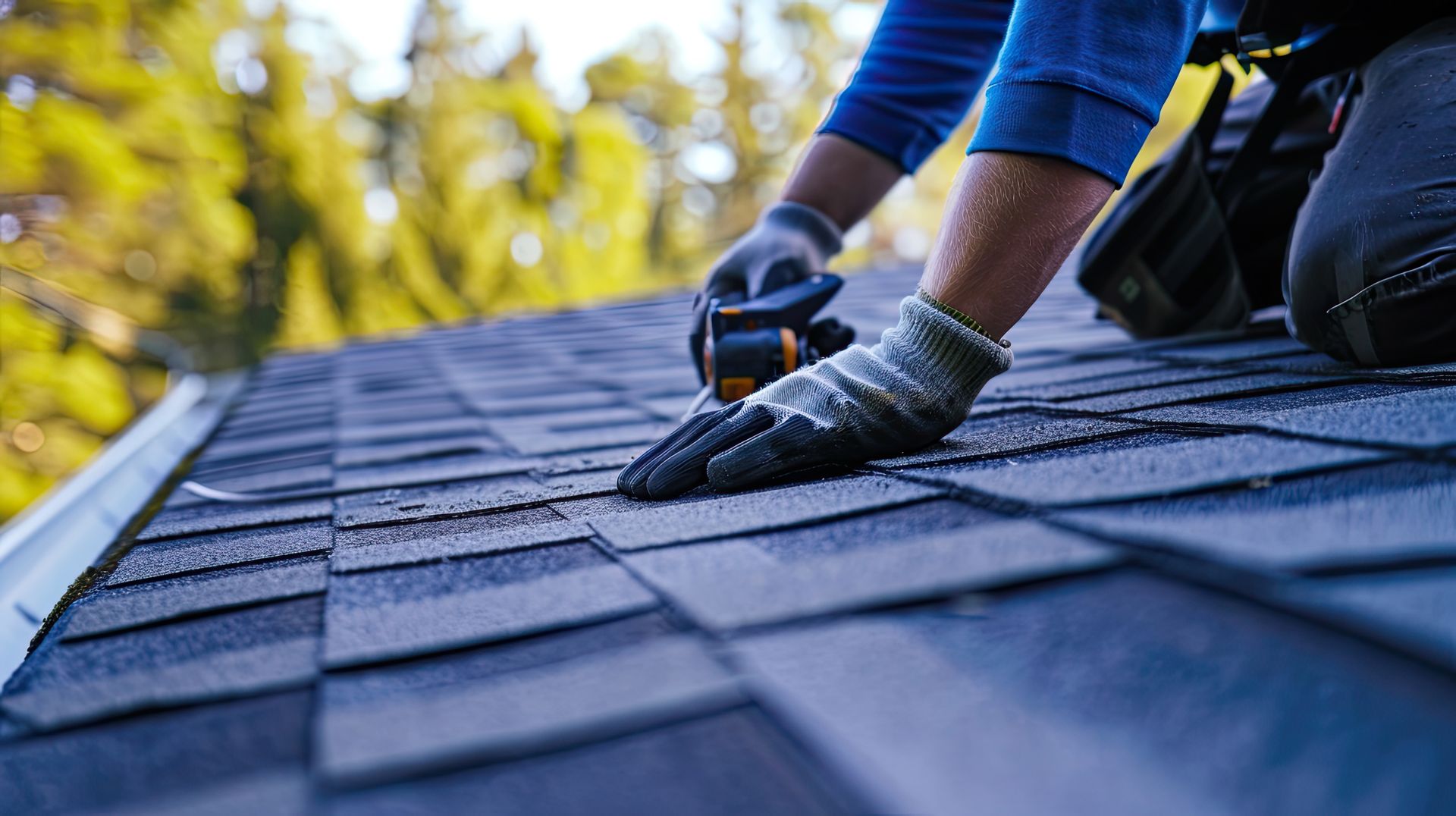 Residential roofing company worker repairing dark asphalt shingles on residential rooftop.