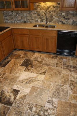 A kitchen with a tile floor , wooden cabinets , a sink and a dishwasher.