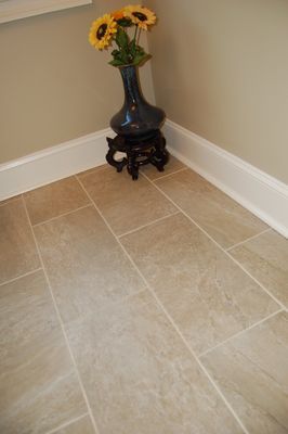 A vase of sunflowers is sitting on a tiled floor next to a wall.