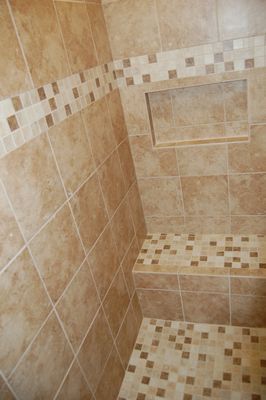 A shower with tiled walls and a shelf in the corner.