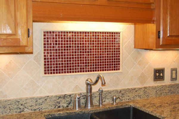 A kitchen sink with a tiled window above it and a faucet.