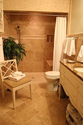 A bathroom with a toilet , sink , and chair.