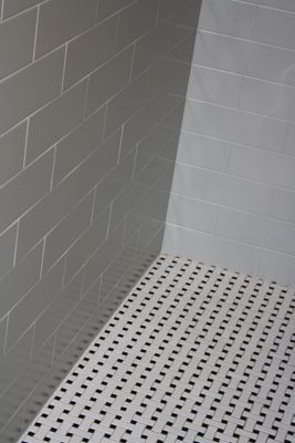A shower with white tiles and black squares on the floor.