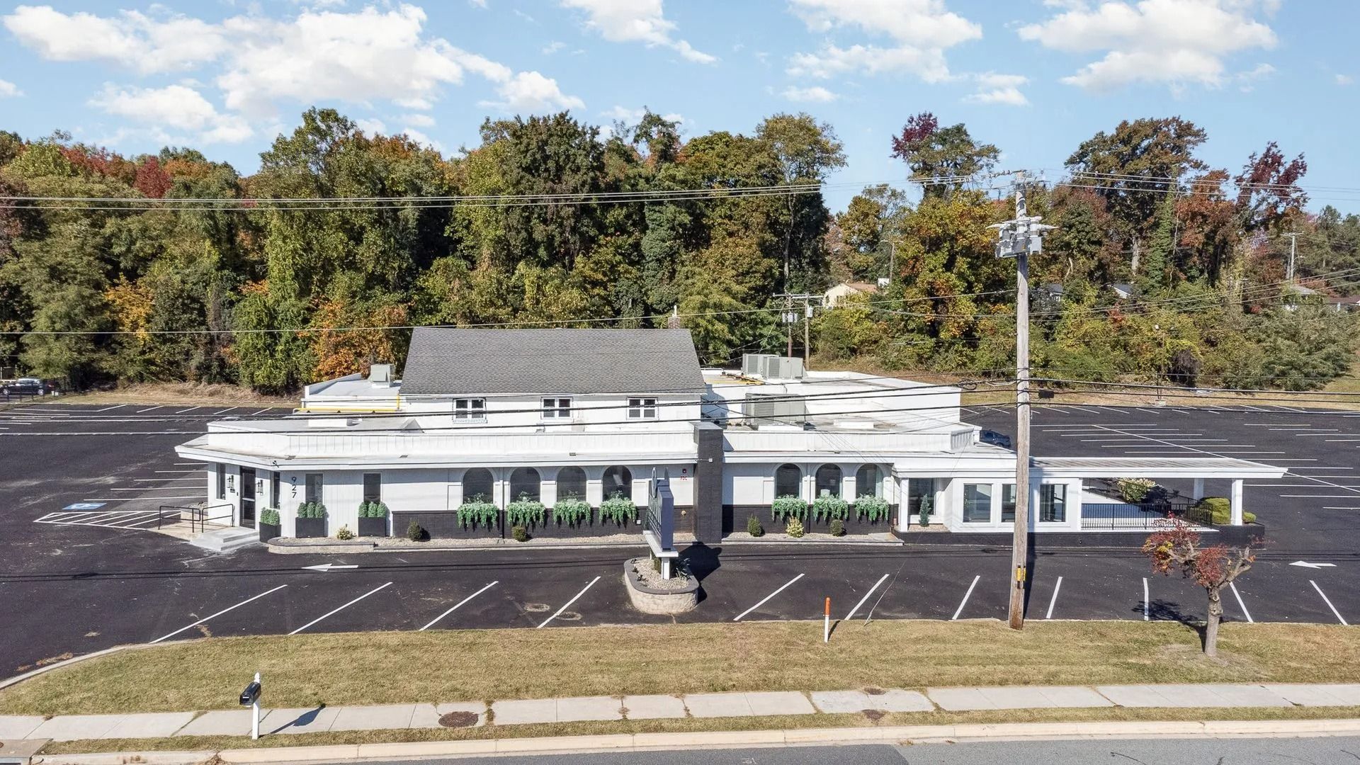 Abandoned one-story commercial building with many windows and a large parking lot in front. Trees in the background.