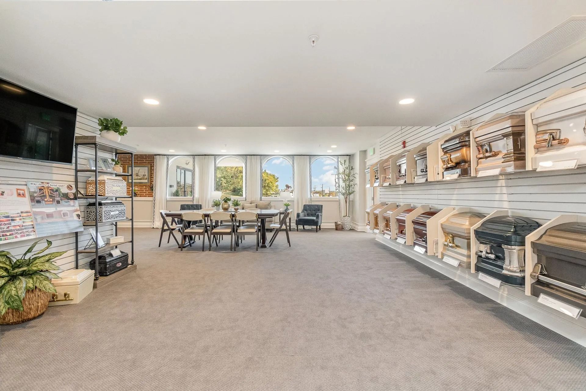 Funeral home interior with display of caskets along the right wall. Meeting table and chairs are in the center.