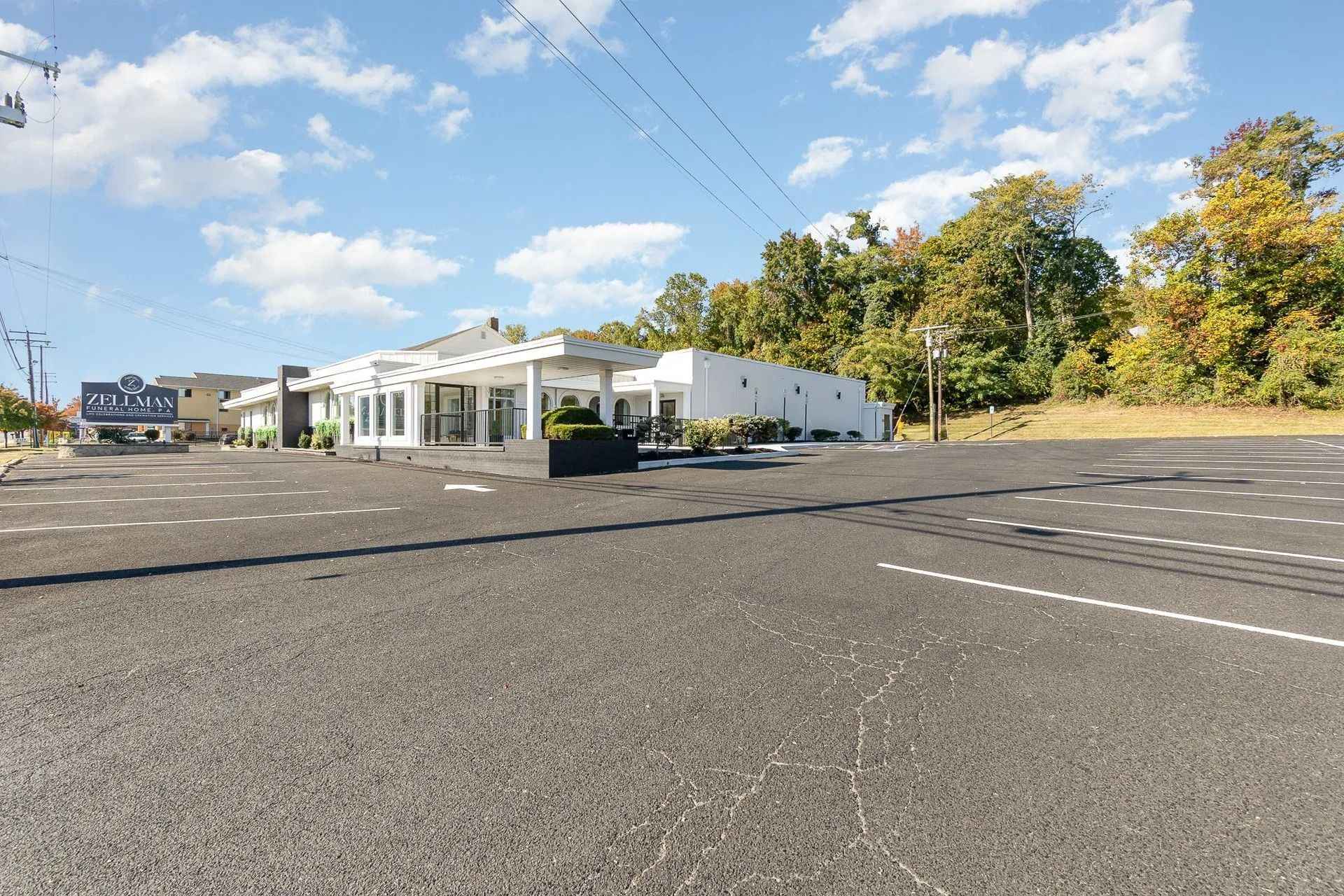 Exterior view of a modern white building with large windows and a paved parking lot on a sunny day.