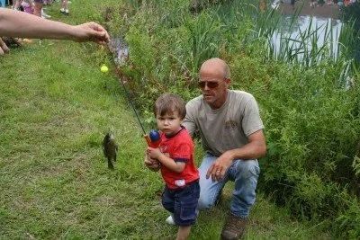 Man and child fishing by a pond, child holding the pole, fish on the line.