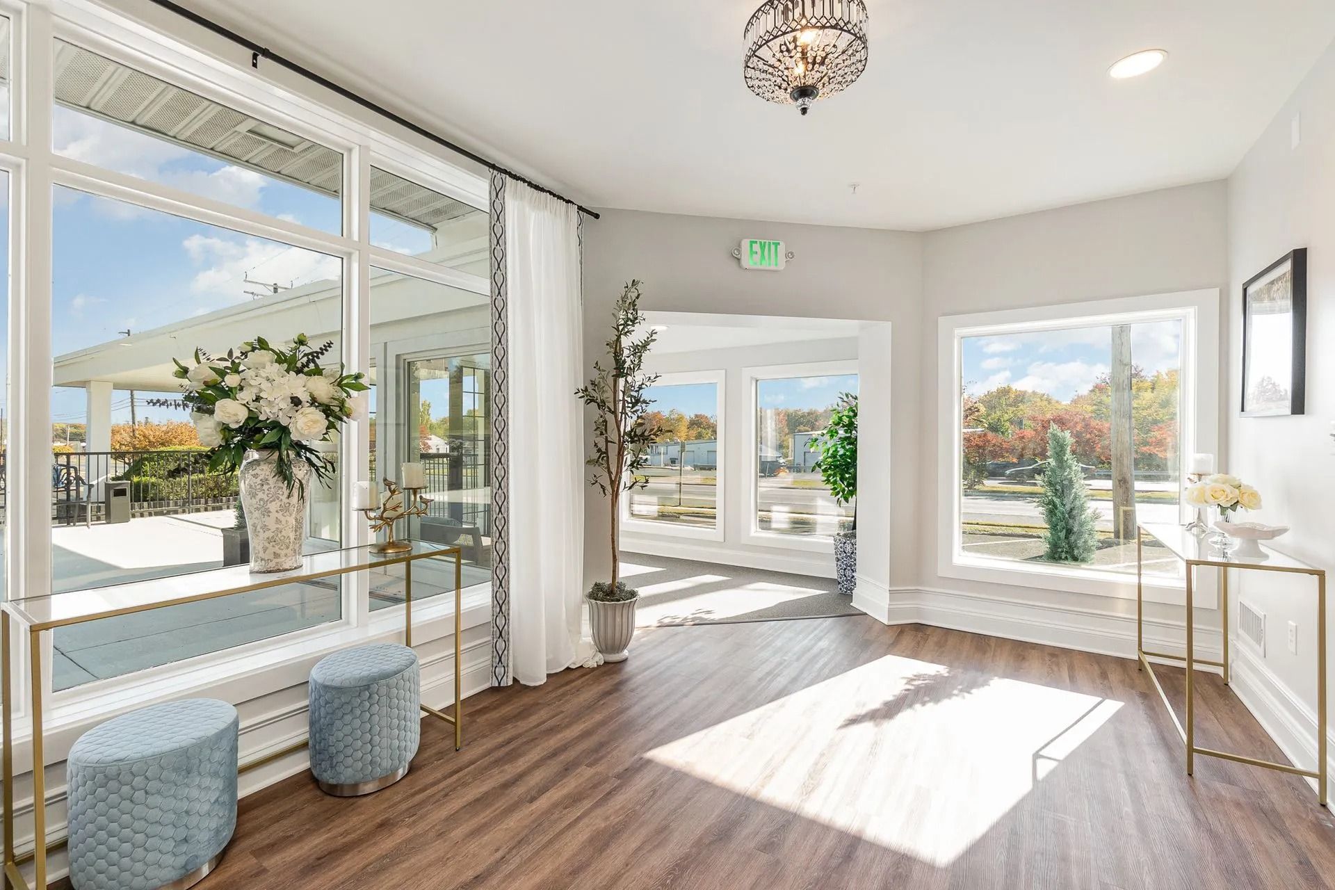 Lobby with large windows, sunlight, and floral arrangements. Includes side tables and decorative stools.