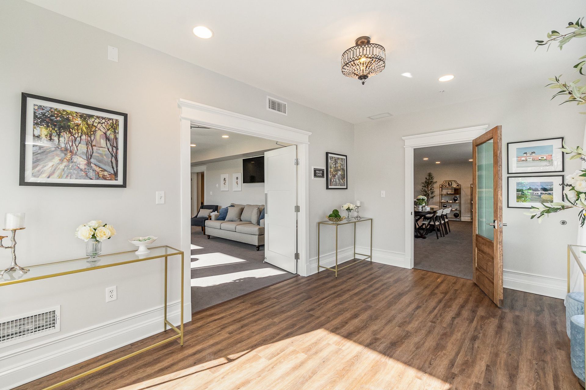 Hallway with open doorways to living and dining areas, featuring hardwood floors and gold accents.