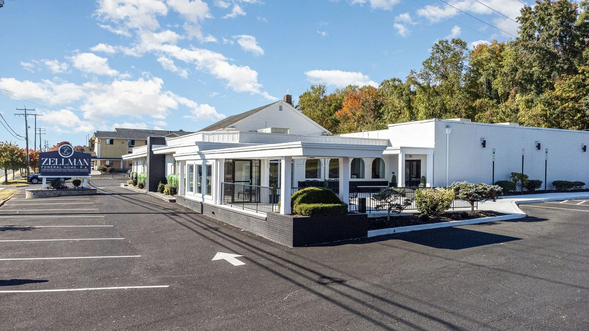White building with columns and windows, black trim, and parking lot on a sunny day.