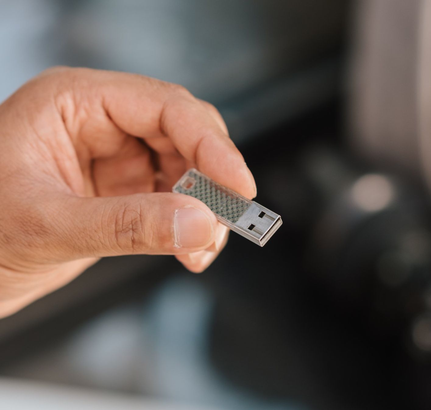 Hand holding a small USB flash drive; blurred background.