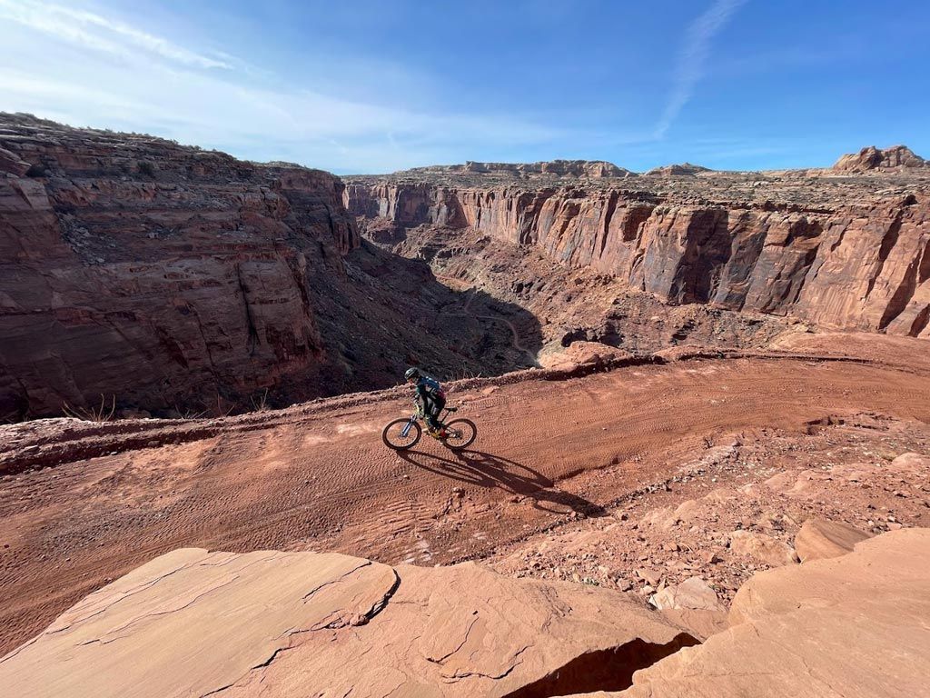 Silhouette of cyclist on a mountain bike against a golden sunset, riding on a dirt trail.