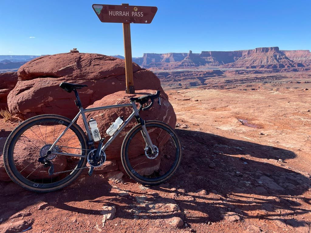 A bicycle rests near a signpost atop a red rock formation, overlooking a canyon.
